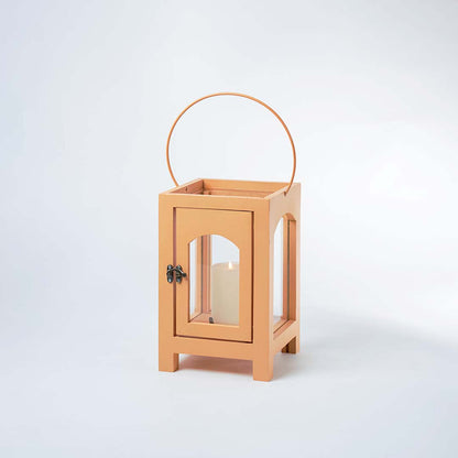 A modern lantern shown on a white background with the inner candle light on creating a warm glow that highlights the clear glass panels and smooth matte finish of the frame.
