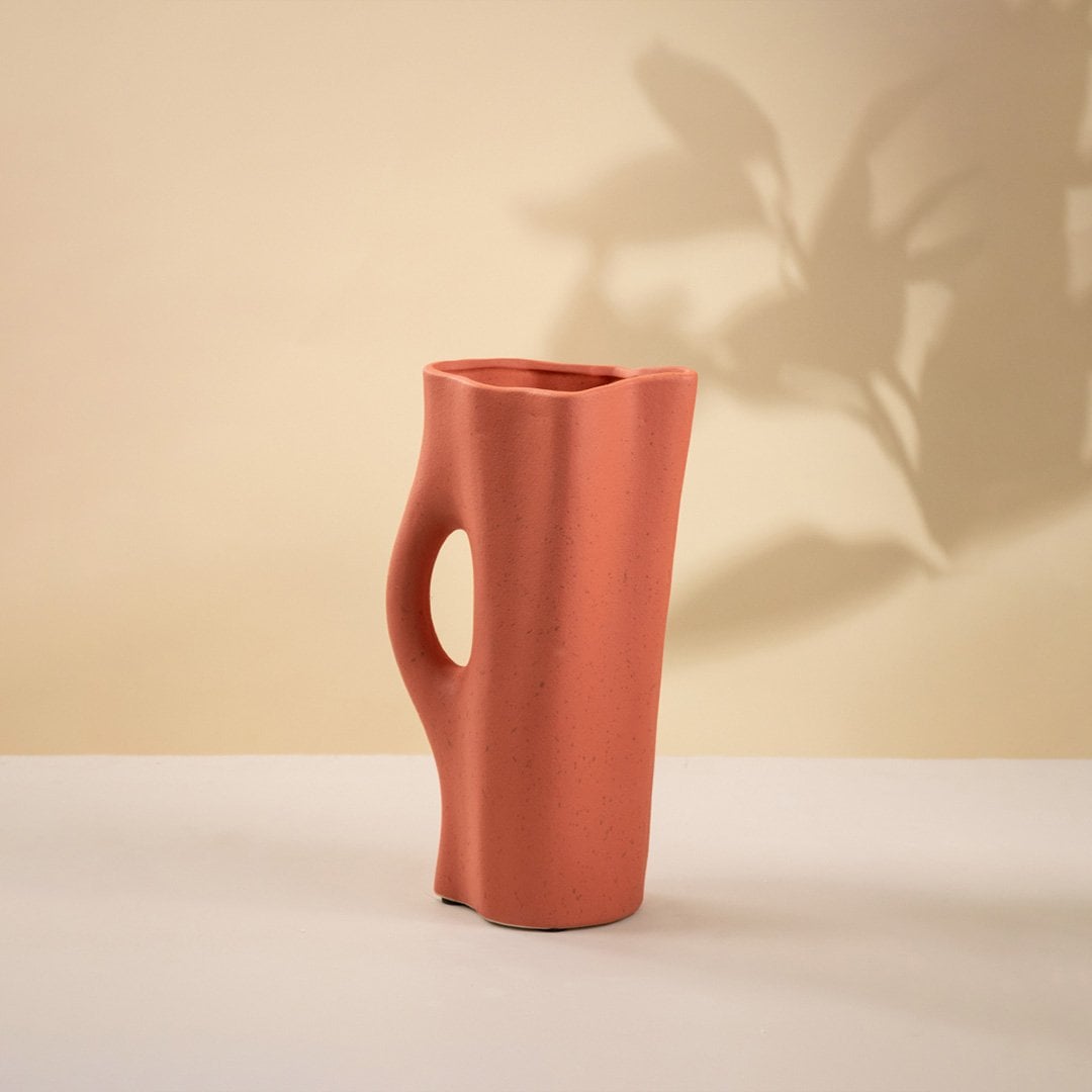 Contemporary terracotta ceramic vase with matte surface and sculpted handle-style cutout placed on a plain white background.