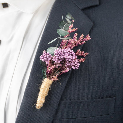Closeup of boutonniere with purple artificial berries and dried flowers wrapped in jute on suit lapel.