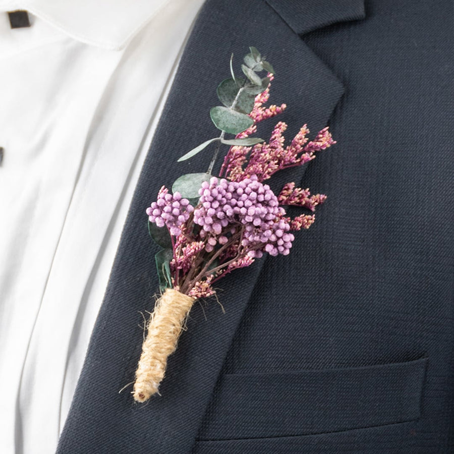 Closeup of boutonniere with purple artificial berries and dried flowers wrapped in jute on suit lapel.