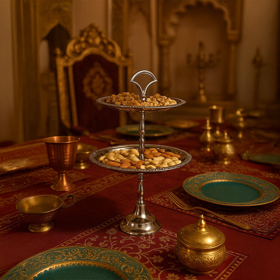 A two tier silver stand filled with assorted nuts displayed on a regal red and gold dining table setting with ornate decor creating an elegant lifestyle scene.