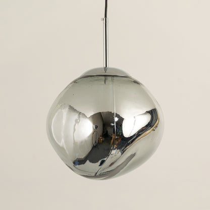 Stylish chrome dome pendant light with reflective metallic finish suspended against beige wall background perfect for luxury modern interior decor.