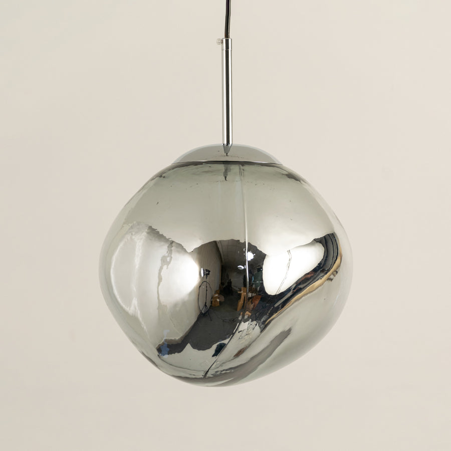 Stylish chrome dome pendant light with reflective metallic finish suspended against beige wall background perfect for luxury modern interior decor.