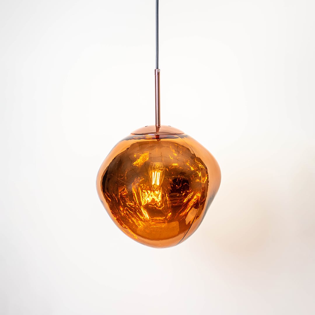 Amber glass globe pendant light turned on with glossy finish and copper hanging rod displayed on a white background.
