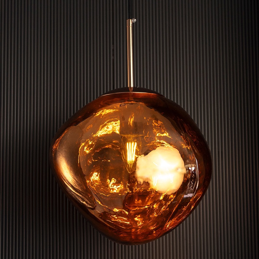 Amber glass globe pendant lamp glowing beautifully with soft golden illumination highlighting its sculptural glass shape.