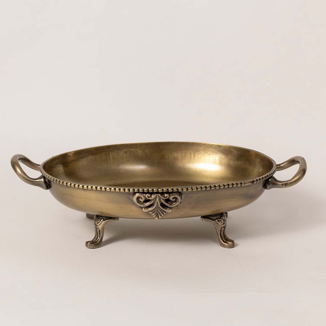 Antique brass serving bowl with engraved detailing and handles placed on white surface against neutral background highlighting traditional decor appeal.