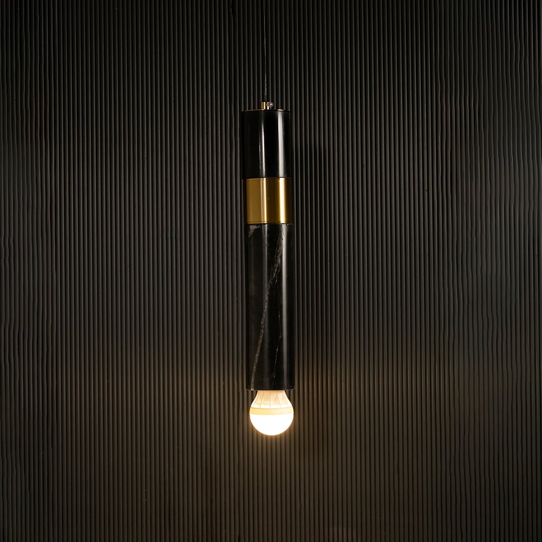 Black marble and metal cylinder pendant light with exposed bulb hanging against dark textured wall with light on for sleek contemporary décor.