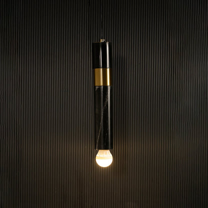Black marble and metal cylinder pendant light with exposed bulb hanging against dark textured wall with light on for sleek contemporary décor.