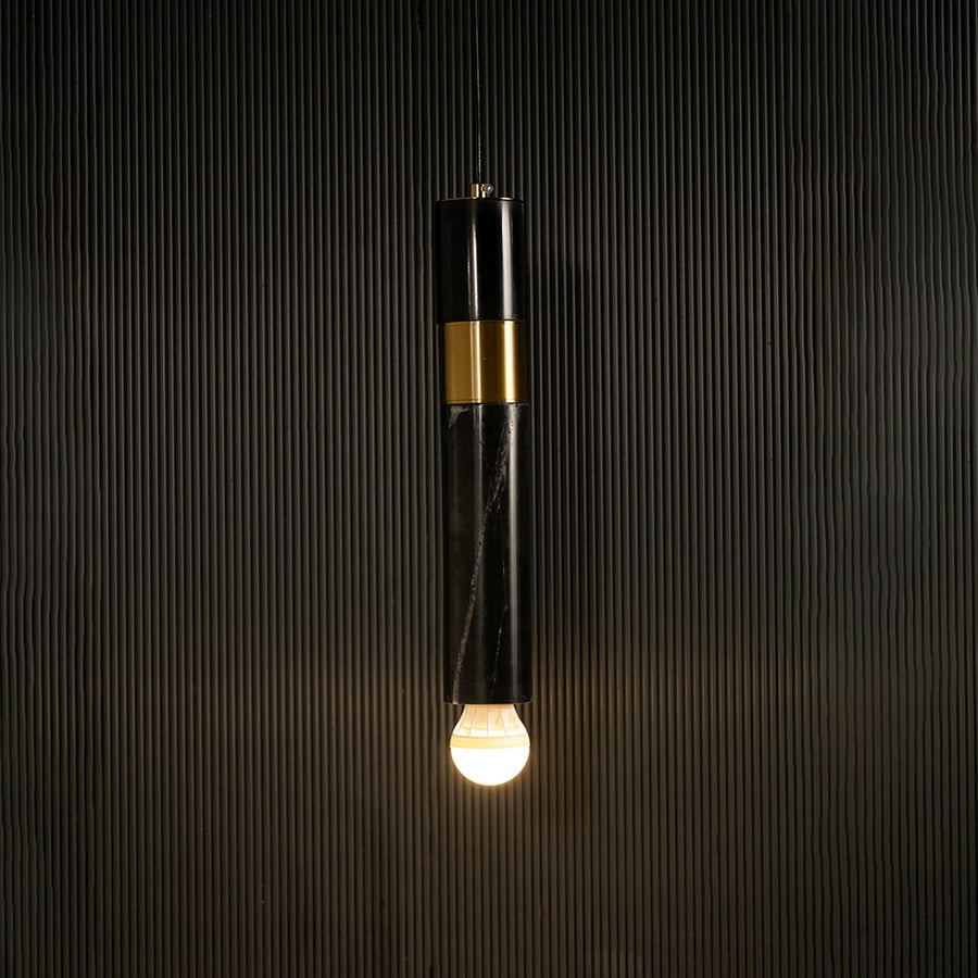 Black marble and metal cylinder pendant light with exposed bulb hanging against dark textured wall with light on for sleek contemporary décor.