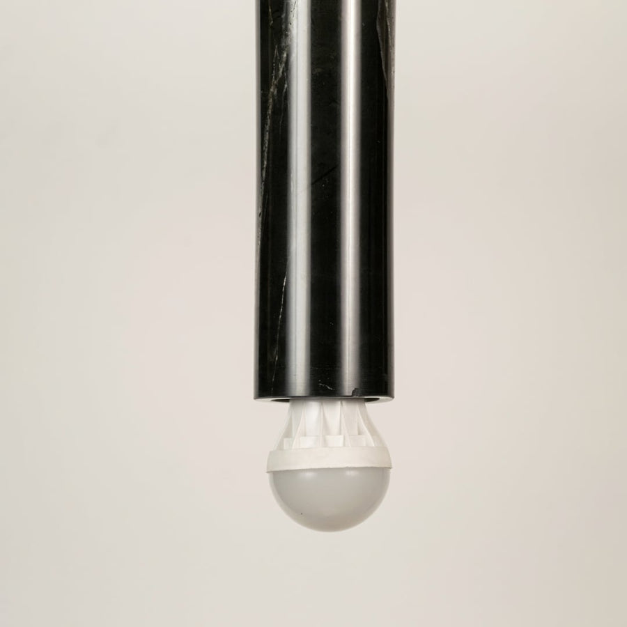 Black marble and metal long cylinder pendant light with clear bulb tip shown in close up view with light off for sleek modern décor.