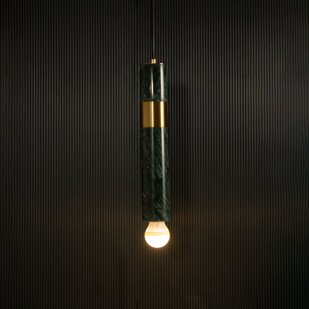Green marble and metal cylinder pendant light with exposed bulb hanging against dark textured wall with light on for luxury modern décor.