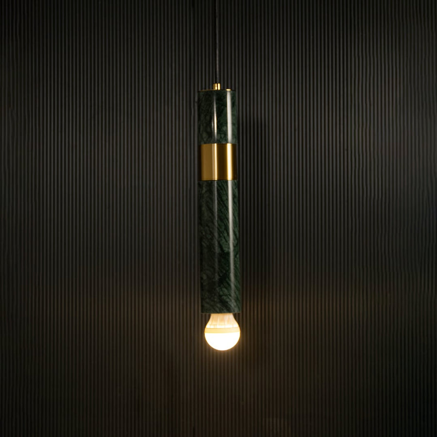 Green marble and metal cylinder pendant light with exposed bulb hanging against dark textured wall with light on for luxury modern décor.