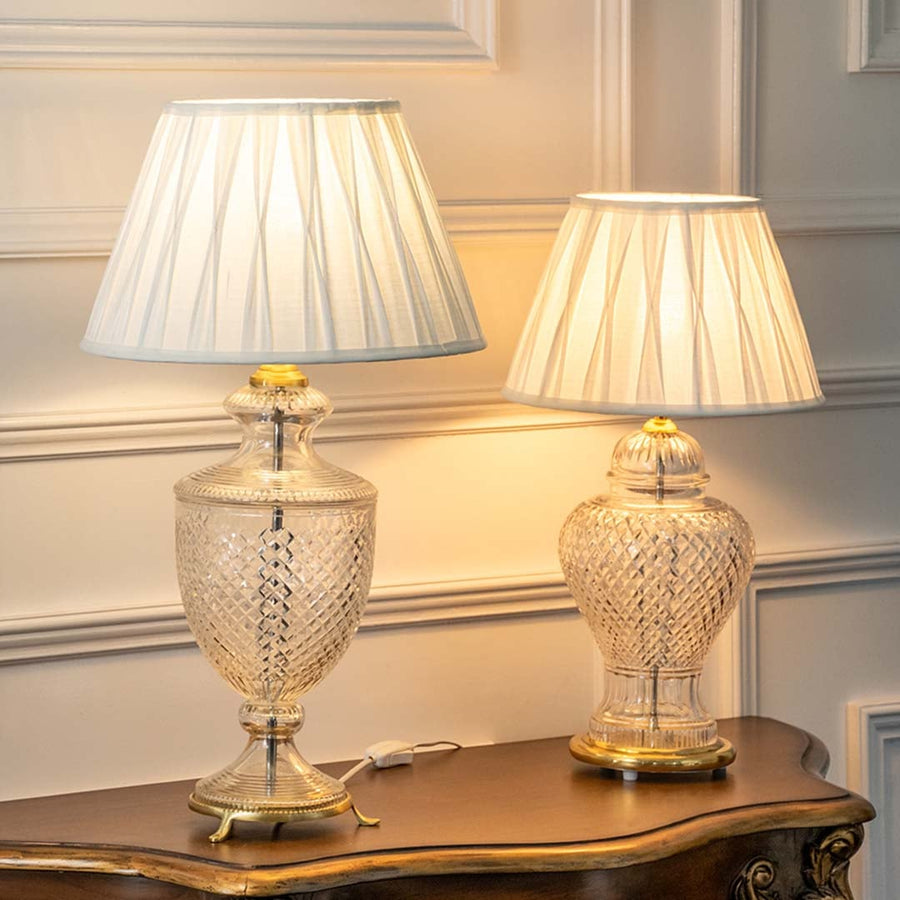 Pair of crystal glass table lamps with pleated fabric shades casting warm ambient light for elegant bedroom decor.