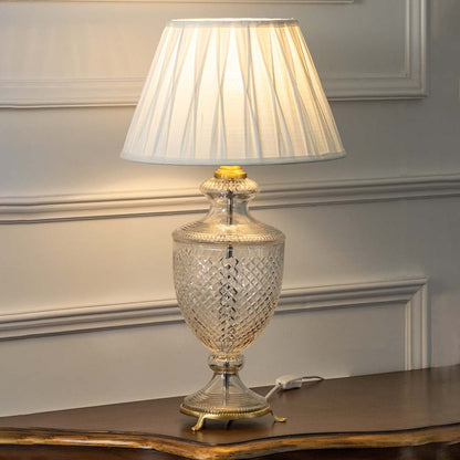 Crystal glass table lamp with pleated shade casting warm ambient light for sophisticated bedroom and living room decor.