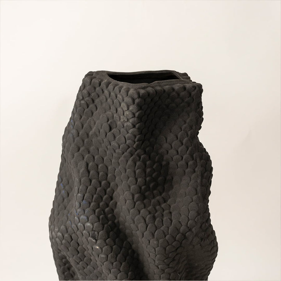 Closeup of black textured ceramic vase highlighting detailed gold dotted accent and handcrafted sculptural surface.