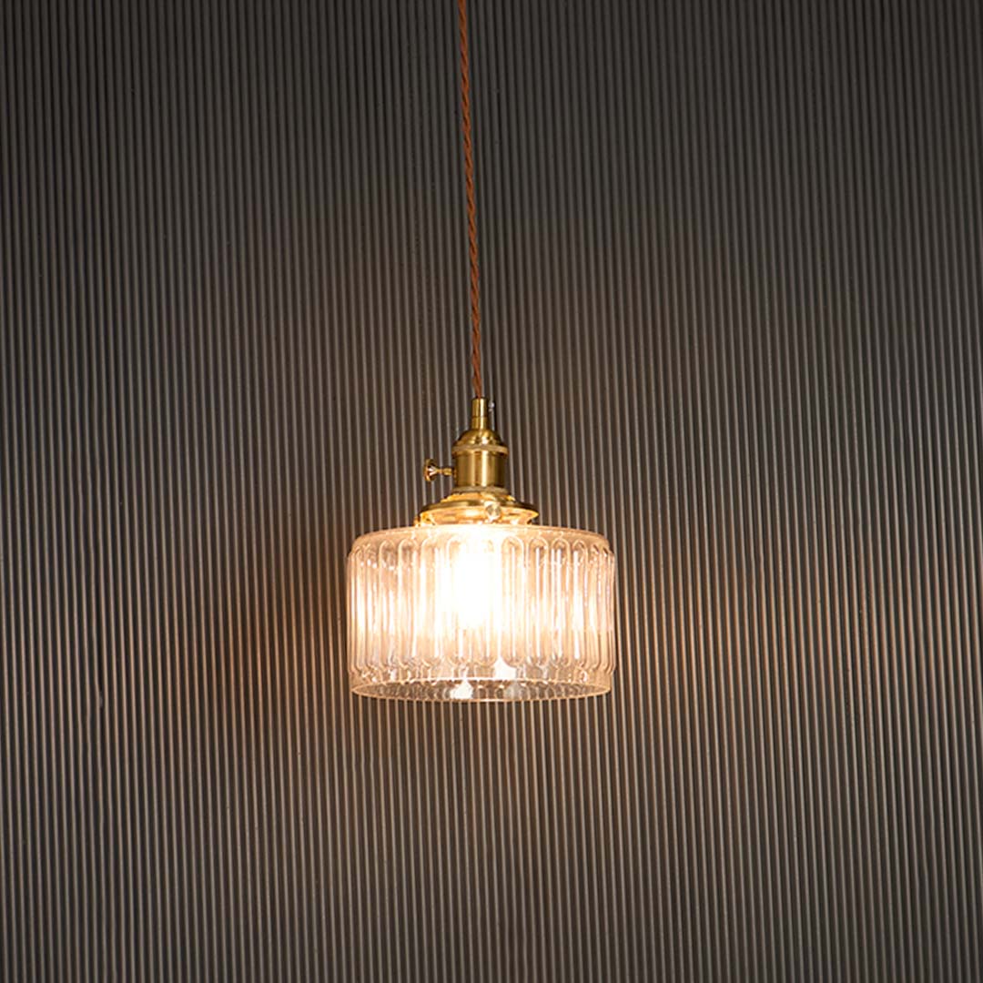 Clear ribbed glass pendant light with brass holder glowing warmly against black background for sophisticated ambience.