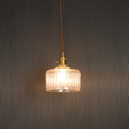 Clear ribbed glass pendant light with brass holder glowing warmly against black background for sophisticated ambience.