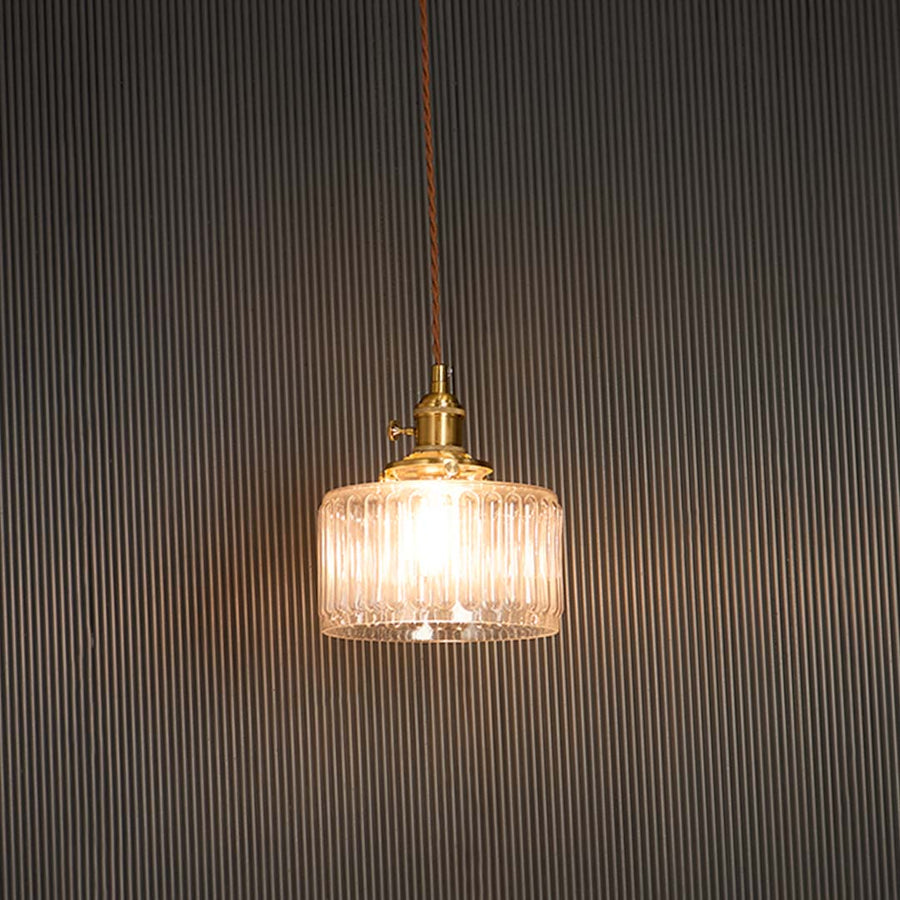 Clear ribbed glass pendant light with brass holder glowing warmly against black background for sophisticated ambience.