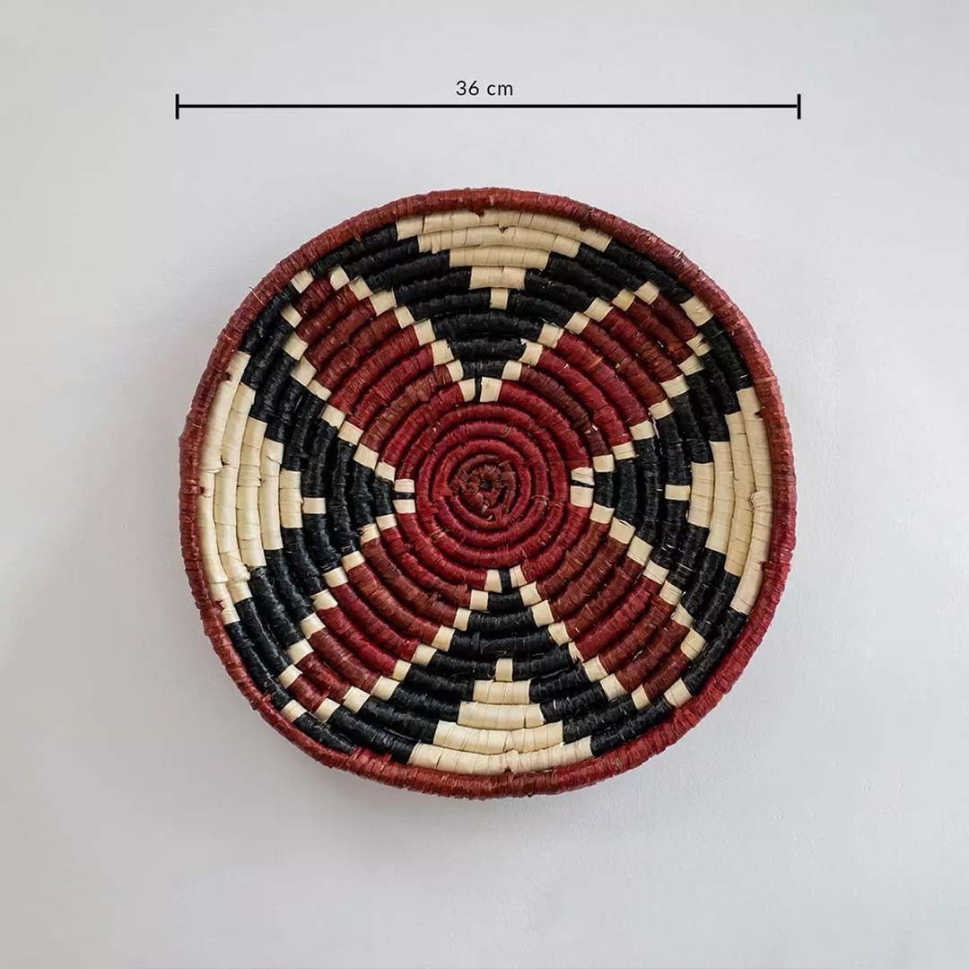 Handwoven round wall basket in red black and natural fiber showing approx thirty cm diameter for interior wall decor placement.