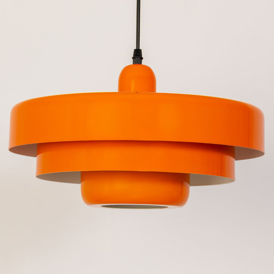 Closeup pendant light in orange metal finish with layered shade design for kitchen or dining decor lighting white background.