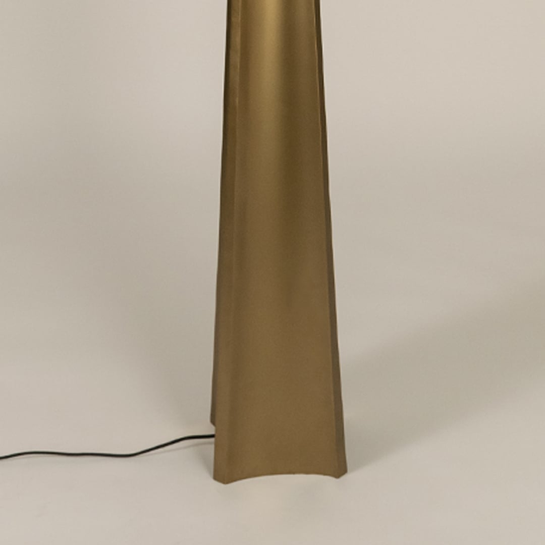 Close up of a tall floor lamp base in a gold finish with a tapered shape and a black power cord resting on a light surface.