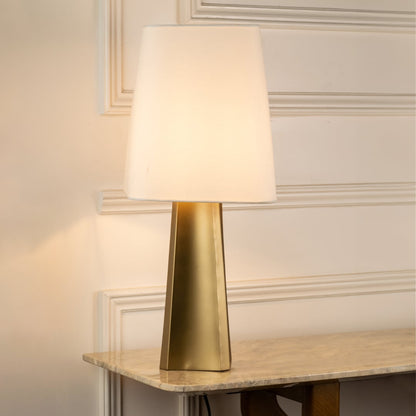 Brass metal table lamp with white fabric shade creating warm ambient lighting for sophisticated interior decor.