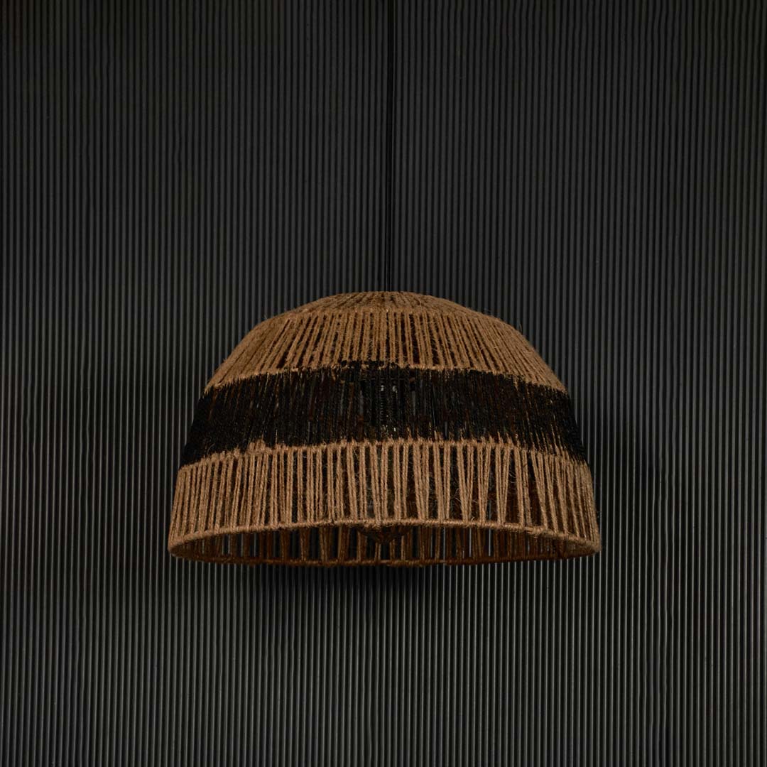 Handwoven jute pendant light with black stripe against dark background highlighting its raw natural texture and artisanal weave.