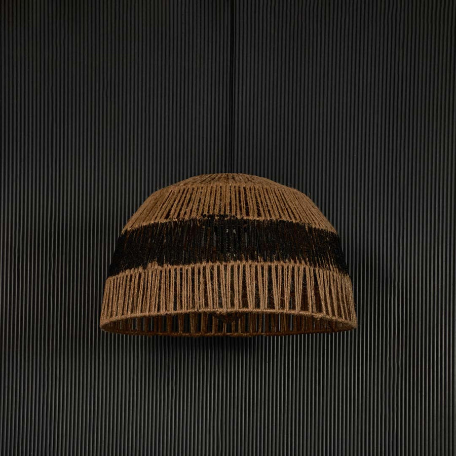 Handwoven jute pendant light with black stripe against dark background highlighting its raw natural texture and artisanal weave.