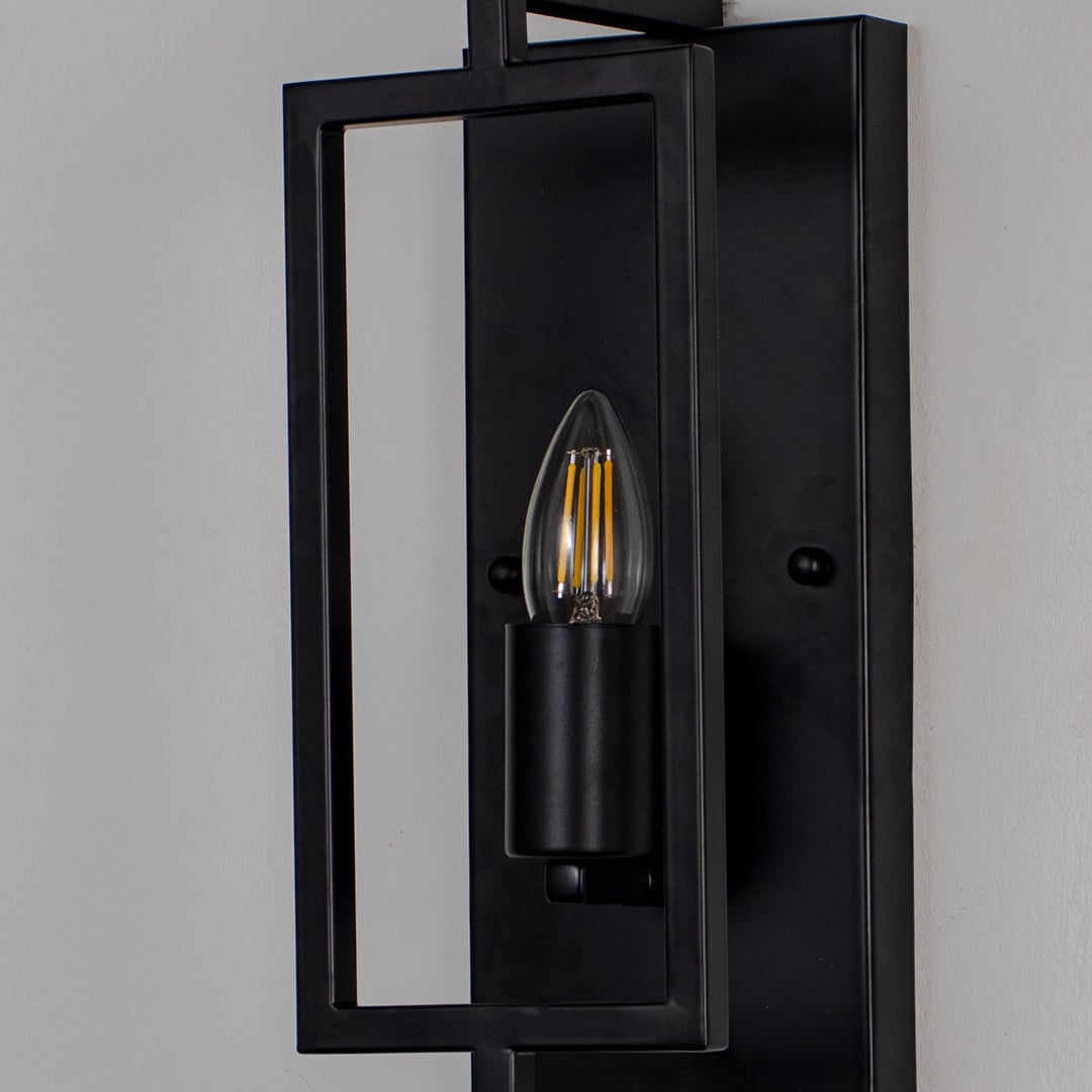 Closeup of wall lamp with sleek black rectangular metal frame and exposed bulb showcasing modern industrial design.