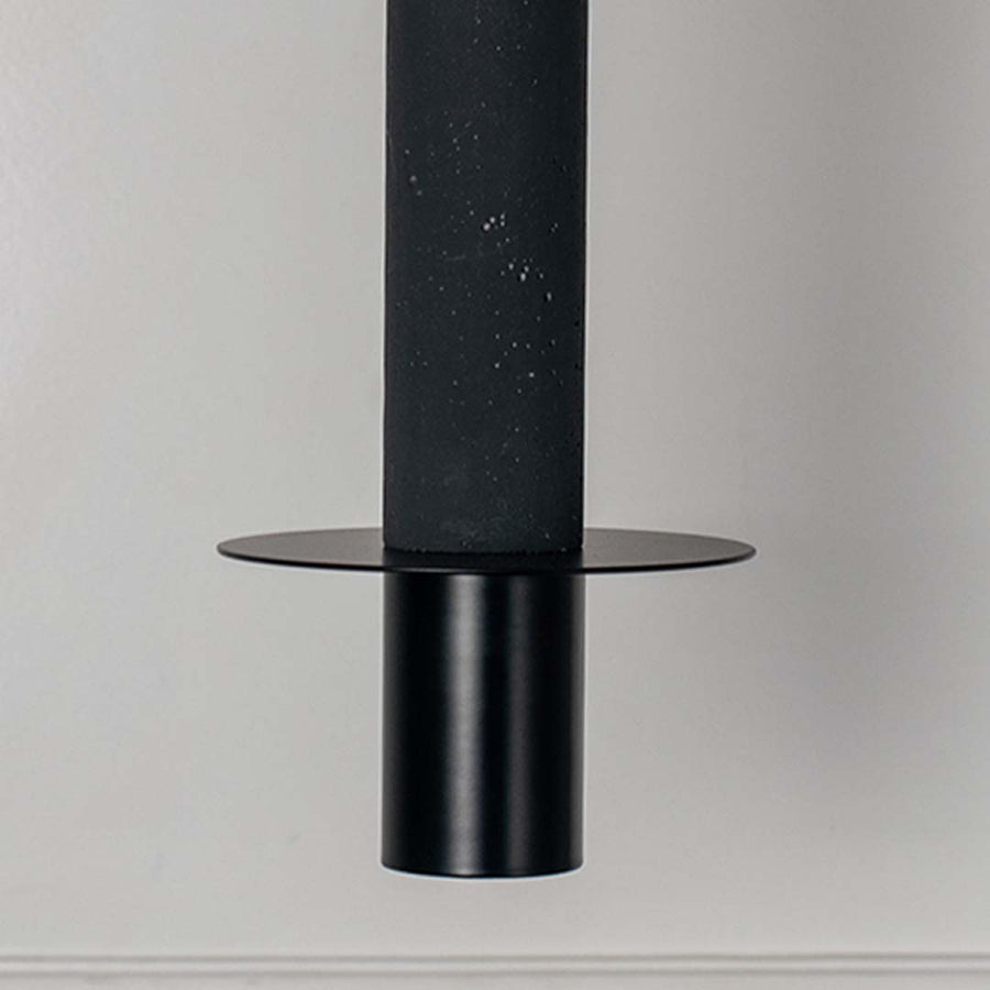 Black cylindrical pendant light with flat disc detail and matte finish hanging against neutral wall background highlighting sleek modern minimal lighting design.