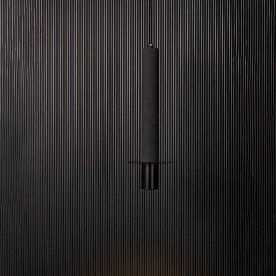 Black cylindrical pendant ceiling light glowing softly against black background creating a modern and elegant interior style.