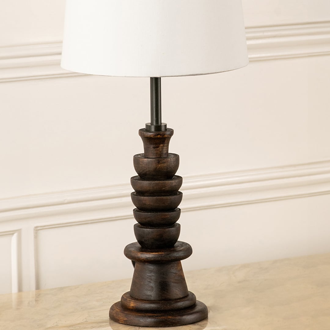 Closeup view of table lamp highlighting its carved dark wooden base and white tapered shade showcasing refined craftsmanship for interior home decor lighting.