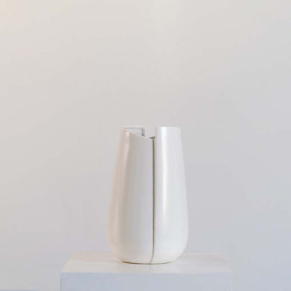 Modern matte white ceramic vase featuring curved abstract slotted panels and open vertical cutouts on white background.
