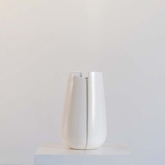 Modern matte white ceramic vase featuring curved abstract slotted panels and open vertical cutouts on white background.