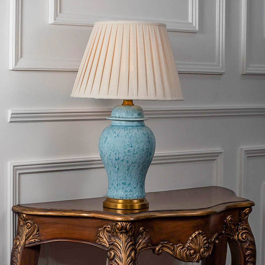 Table lamp with light blue ceramic base and white pleated shade on wooden console table classic lighting for living room decor.