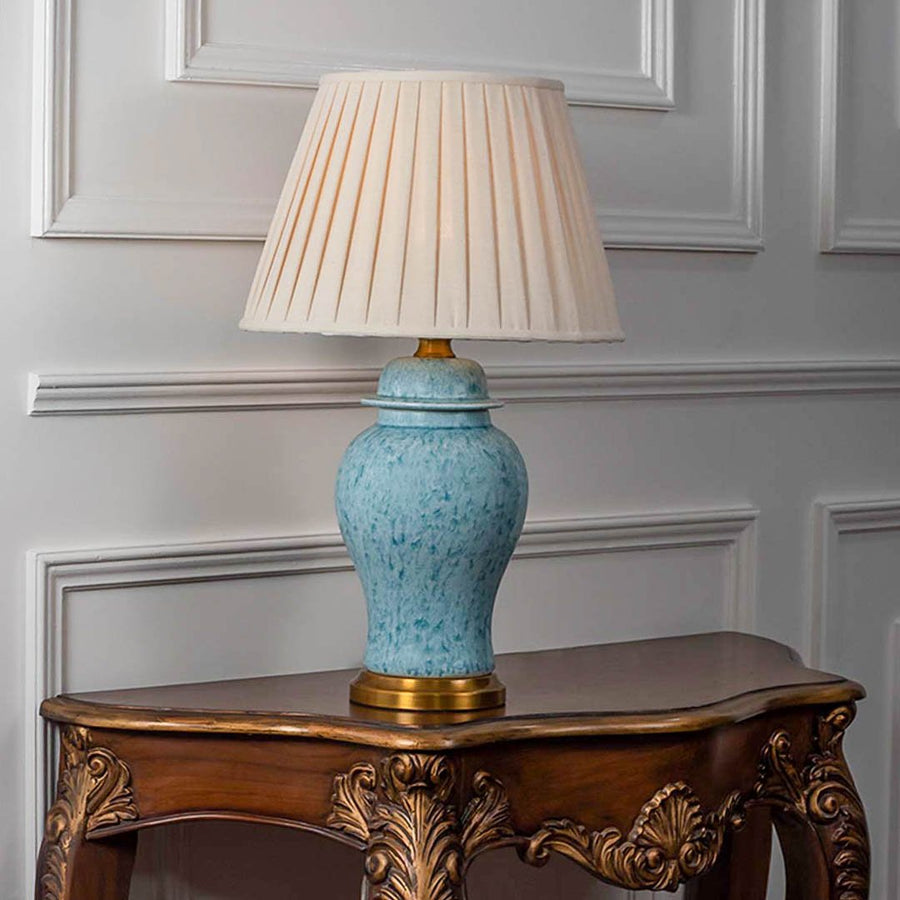 Table lamp with light blue ceramic base and white pleated shade on wooden console table classic lighting for living room decor.