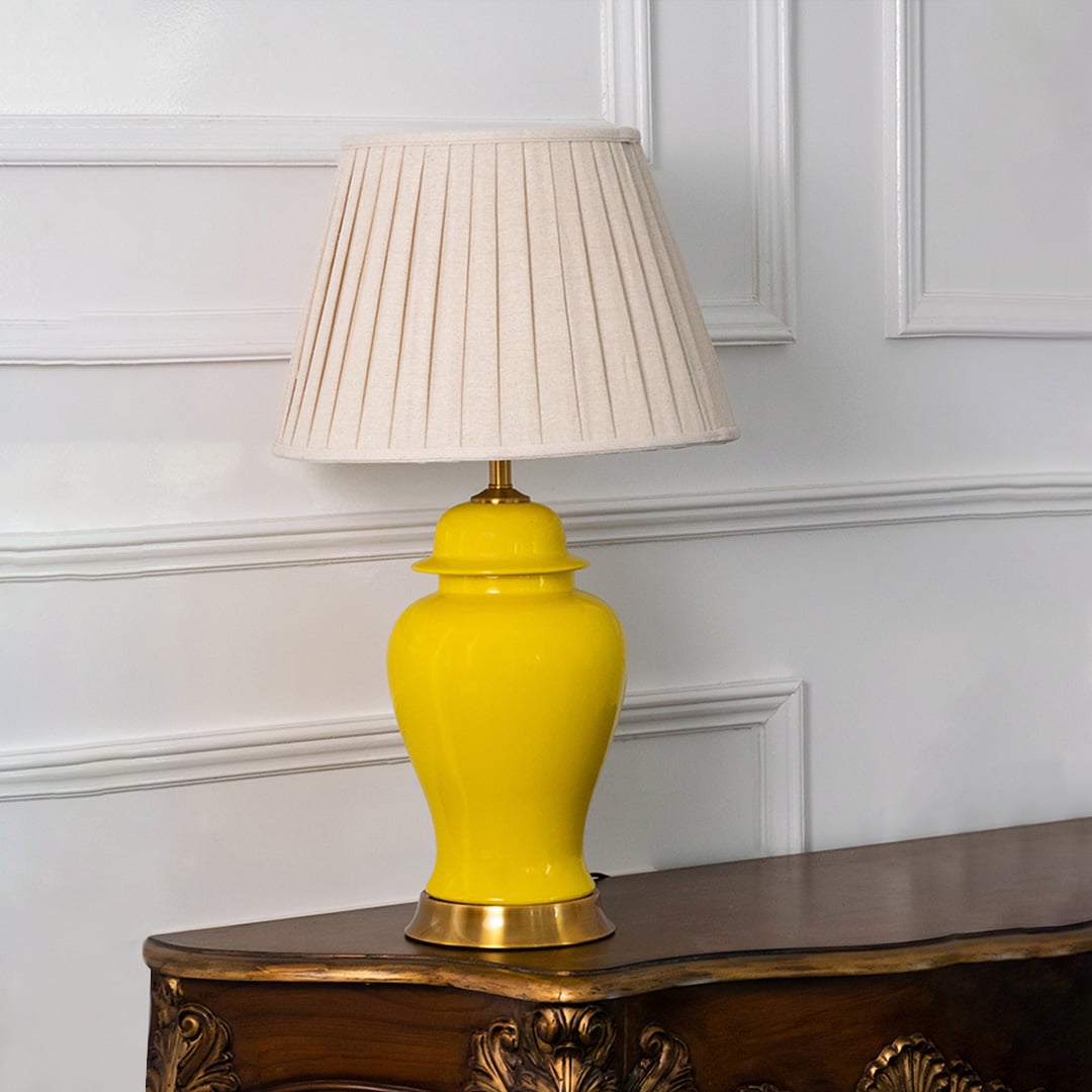 Yellow ceramic lamp with golden base and fabric pleated shade displayed against white background.