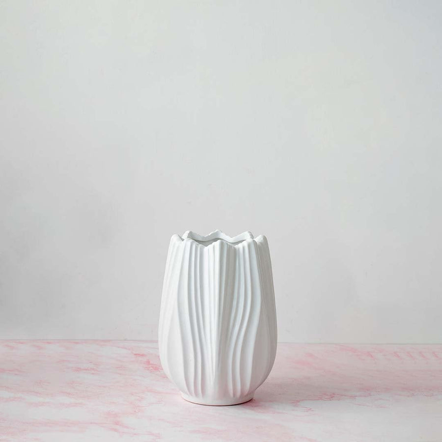 White textured vase on a matte white background with soft shadows emphasizing its curvy design.