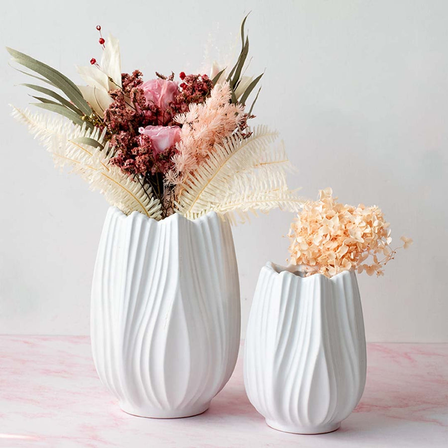 White ceramic vases with sculpted wavy texture displayed together on a soft pink surface filled with dried florals creating a calm modern Decor styling.