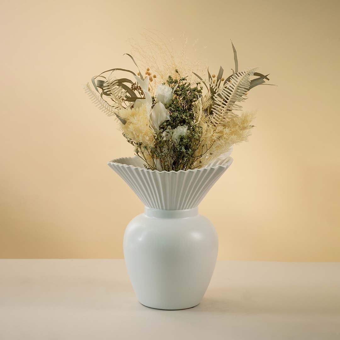 Modern white ceramic vase with pleated design styled with dried floral arrangement on wooden coffee table enhancing the elegant living room decor.