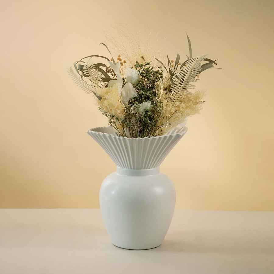 Modern white ceramic vase with pleated design styled with dried floral arrangement on wooden coffee table enhancing the elegant living room decor.
