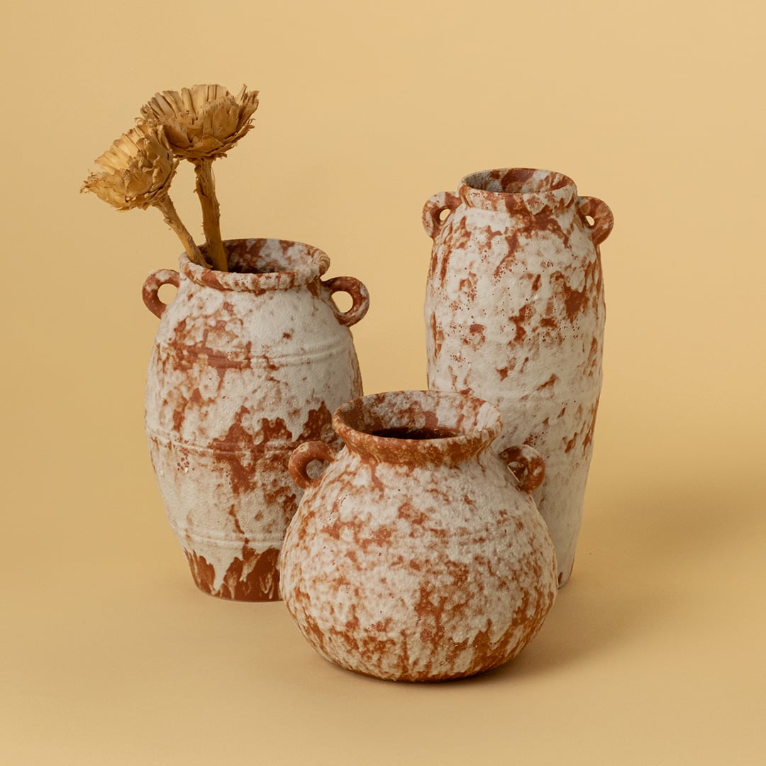 Earthy terracotta ceramic vases in rustic textured finish styled as a group on wooden table for warm home decoration.