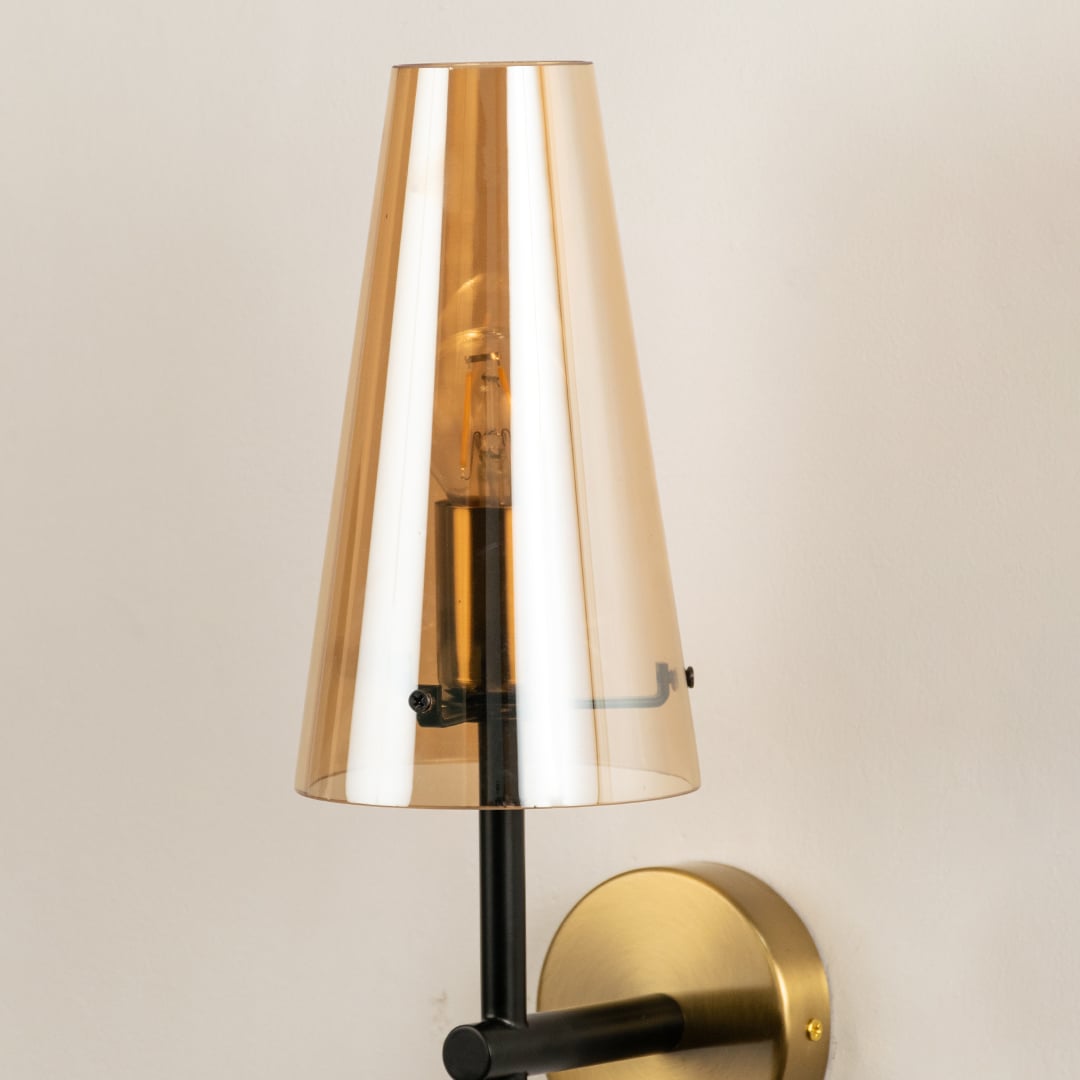 Closeup view of amber glass wall sconce highlighting the warm glow of the bulb and the smooth gold mount with a sleek black stem showing refined detailing and craftsmanship.