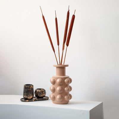 Rust cattail stems styled in textured beige vase for modern home decoration.