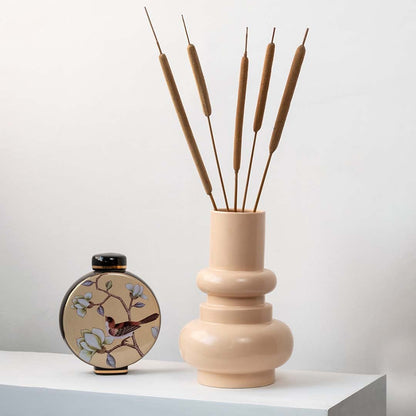 Brown cattail stems styled in beige ceramic vase placed on modern table for elegant home decoration.