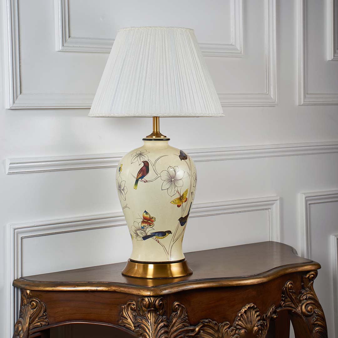 Ivory ceramic lamp with golden base and floral bird artwork displayed with light off against clean white background.
