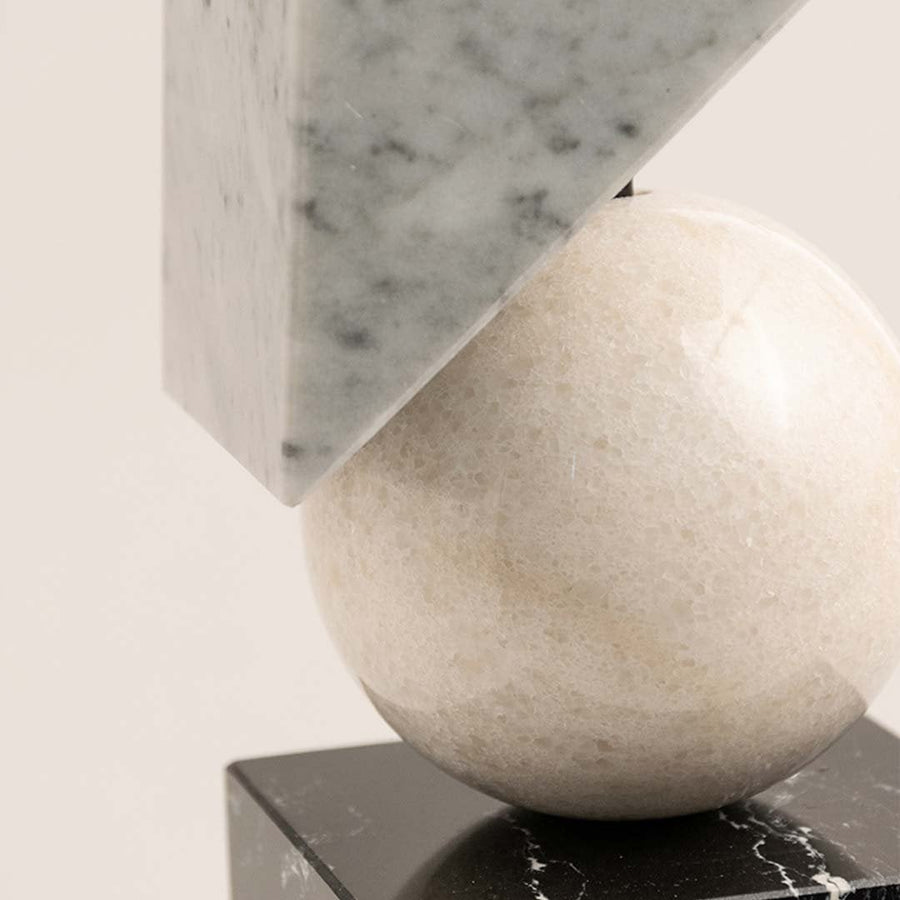 Closeup of marble geometric sculpture showing cube sphere and triangle shapes with polished artistic finish.