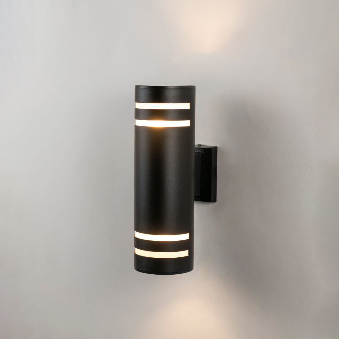 Black metal outdoor wall light glowing on white wall with gold accent bands for elegant exterior decor.