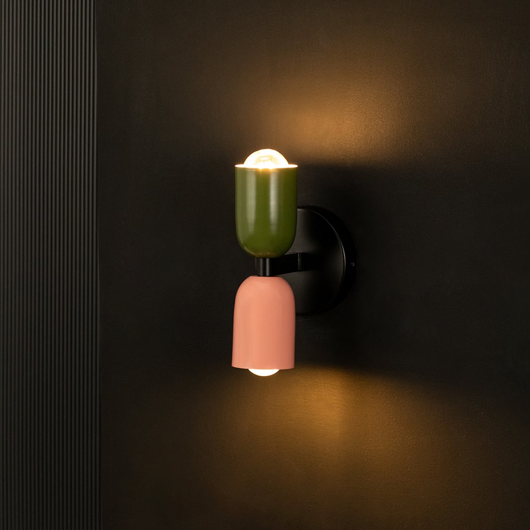 Modern wall light illuminated against dark background highlighting green and peach finish.