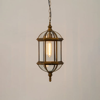 A bronze vintage style hanging lantern lit with a warm glow showcasing its elegant glass panels and dome top design suspended from a chain against a neutral wall backdrop.
